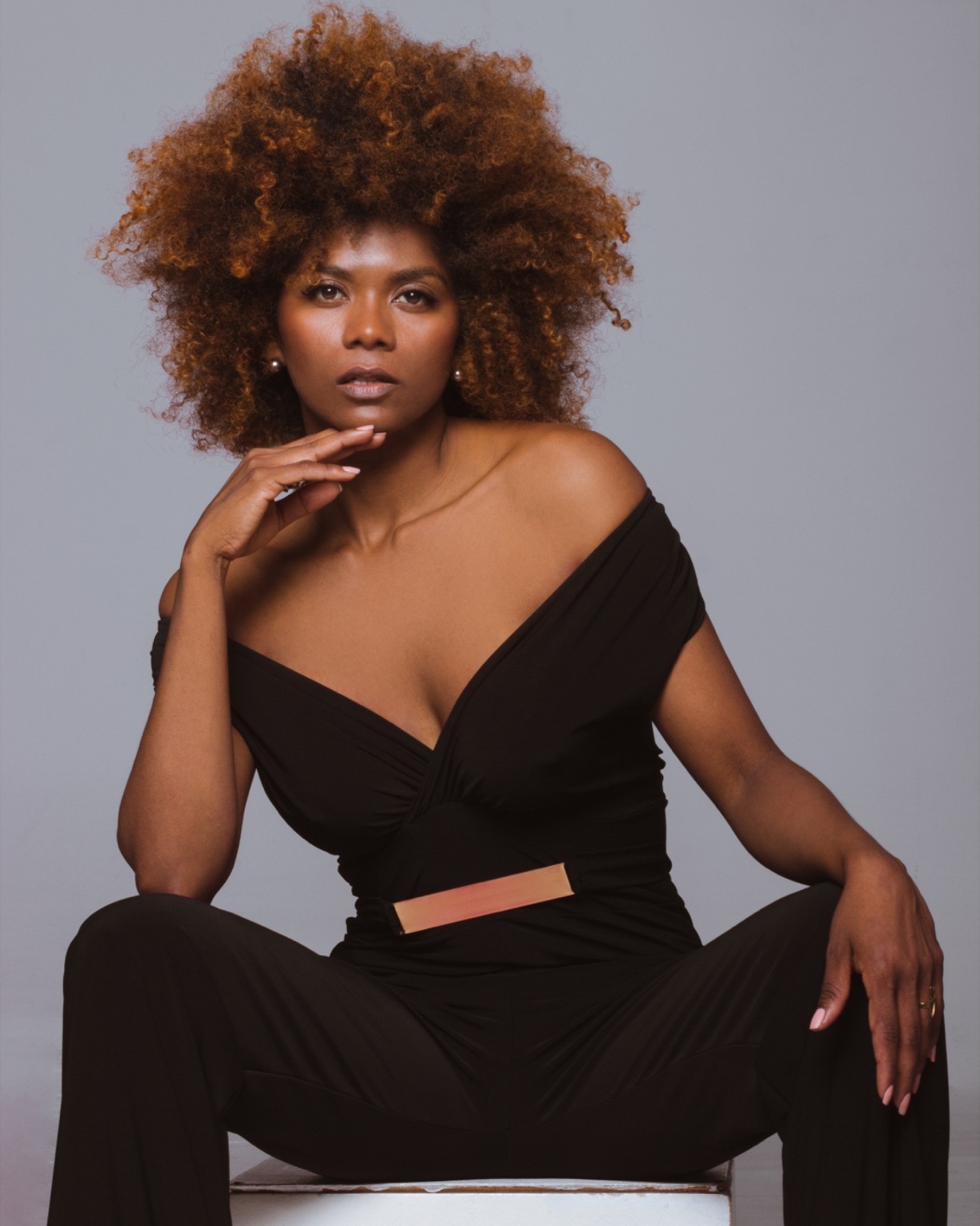 Mirna Franco with her signature curls, wearing black against a grey studio backdrop